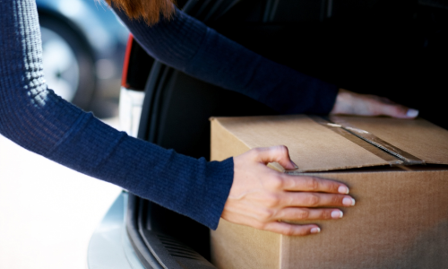 A cardboard box being placed into the trunk of a car.