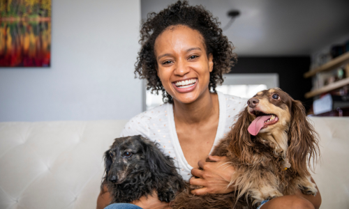 A woman holding her two dogs, smiling on a couch.
